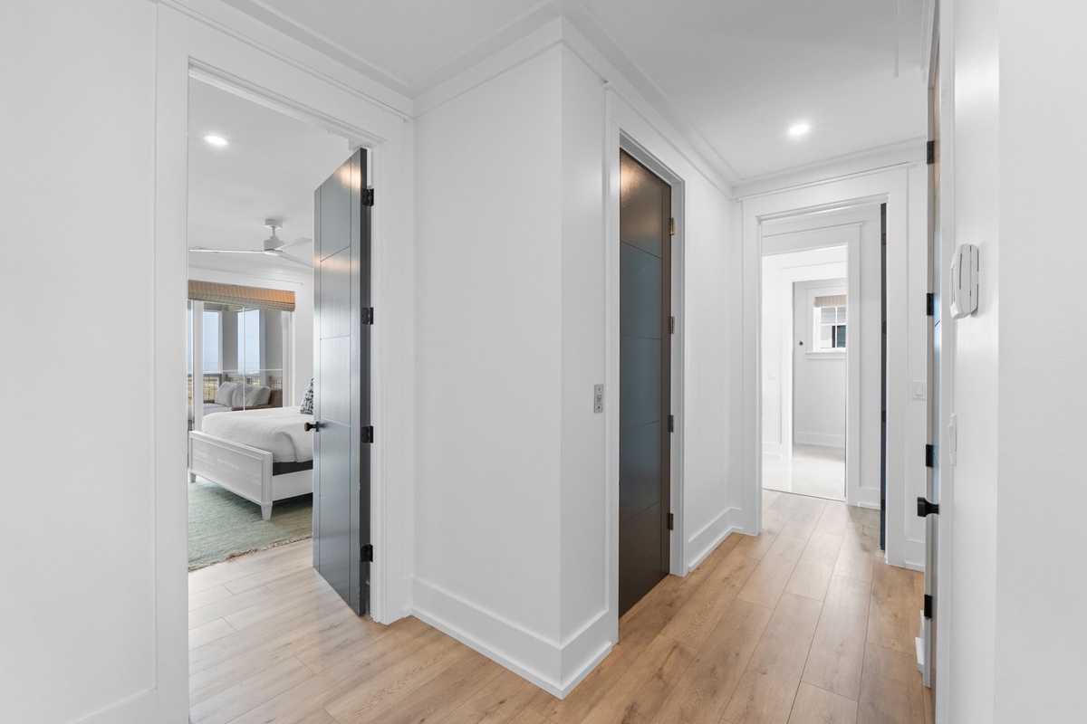 Step into a light-filled hallway where sleek design meets coastal calm. Warm wood floors guide you past thoughtful glass doors, connecting bedroom and bath effortlessly.