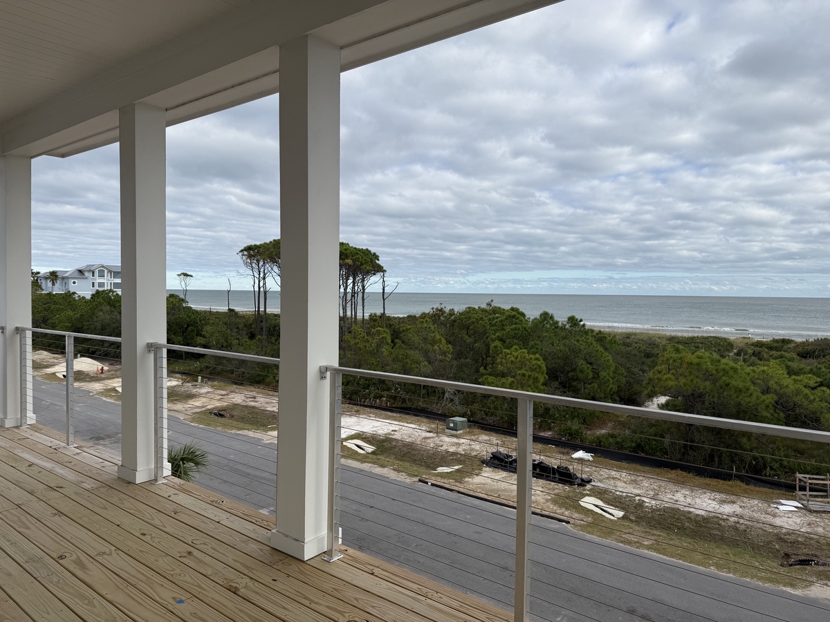 Spacious covered balcony with stunning ocean views through lush coastal forest canopy.