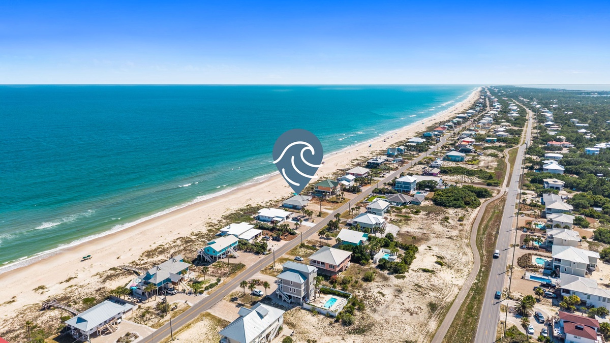 Aerial view capturing the beachfront neighborhood stretching along miles of pristine coastline, showcasing the property's prime location near turquoise waters and sandy shores.