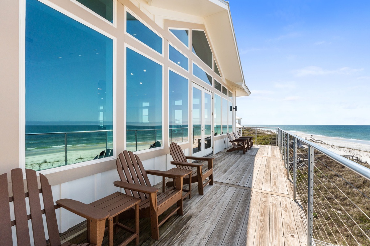 Modern beachfront property featuring expansive glass walls and a wraparound deck overlooking pristine white sand beaches.