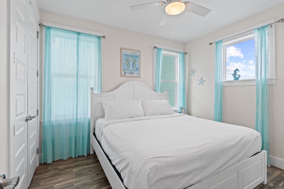 Drift off in your serene coastal bedroom with crisp white linens and calming turquoise accents. Natural light fills the space while gentle ceiling fan breezes keep you comfortable.