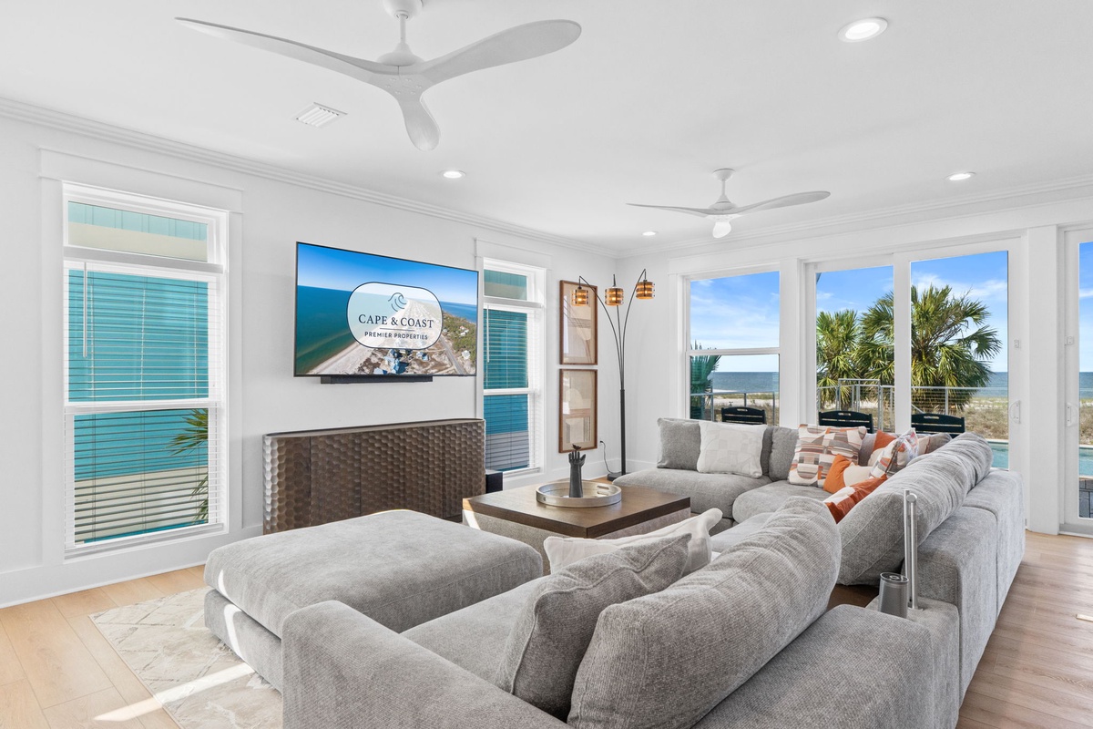 Sink into plush sofas while palm trees frame your ocean view. Ceiling fans keep the sea breeze flowing through this bright, airy living space—your perfect coastal retreat.
