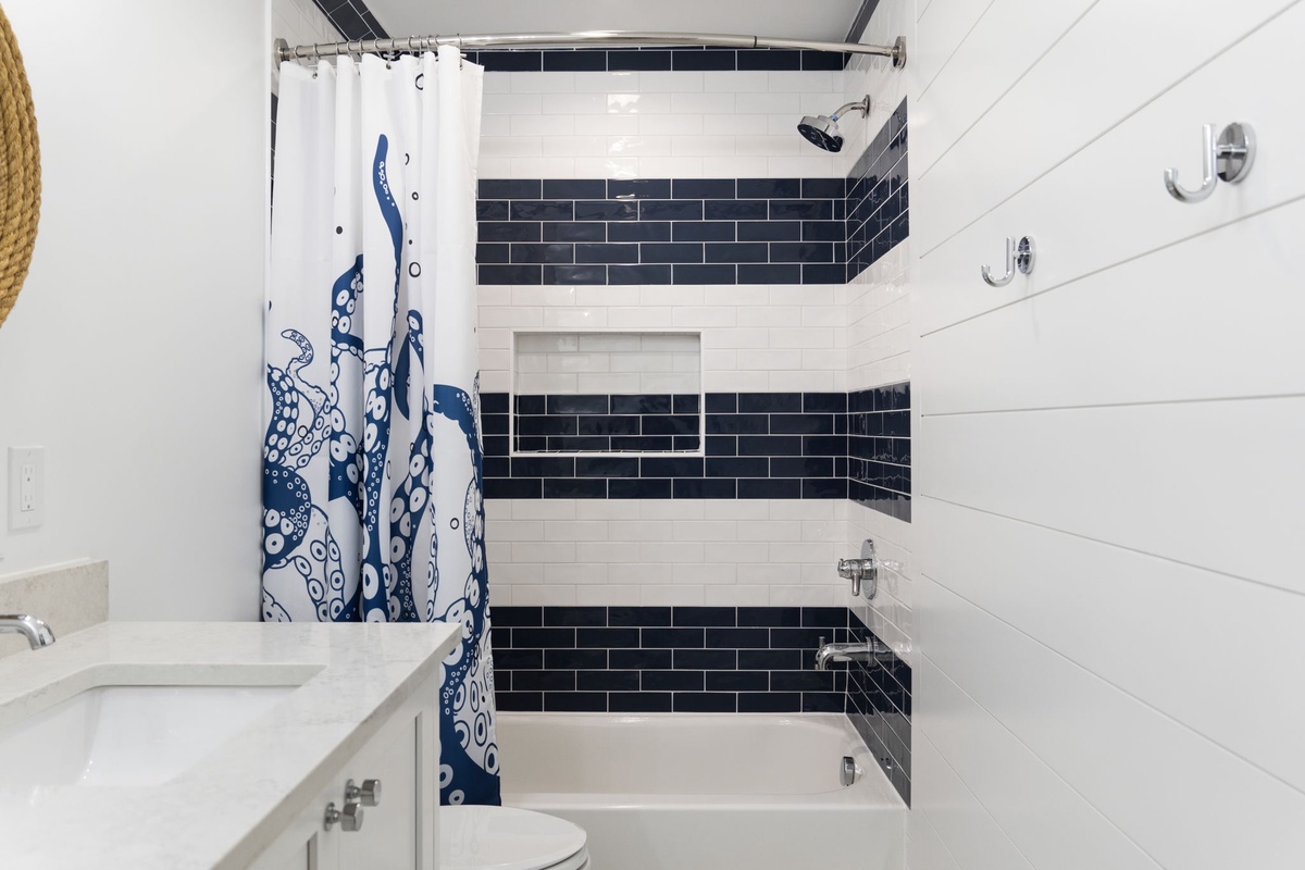 Step into your stylish bathroom featuring a nautical-themed curtain and crisp navy and white subway tiles. Enjoy a refreshing shower or soak in the tub after a day of exploring.