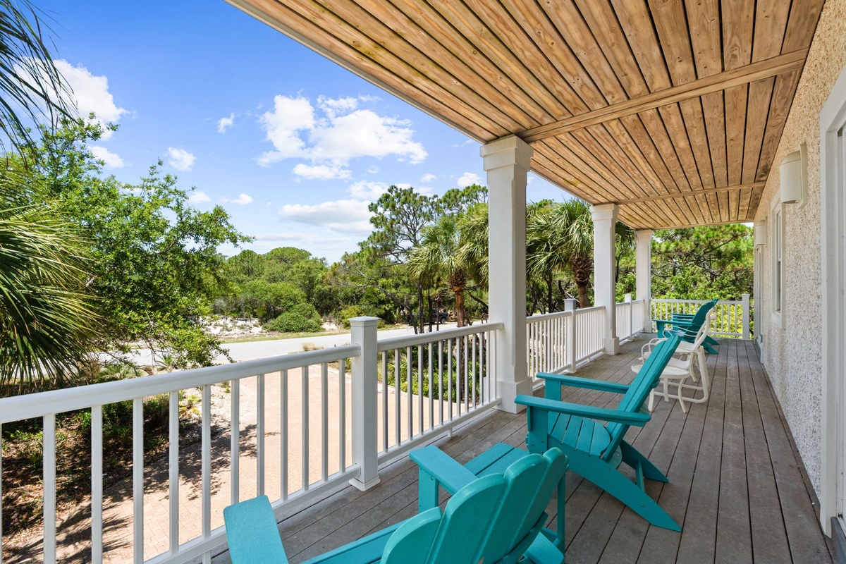Settle into your private covered porch with vibrant turquoise Adirondack chairs, where you can soak in coastal breezes and lush greenery surrounding your peaceful retreat.