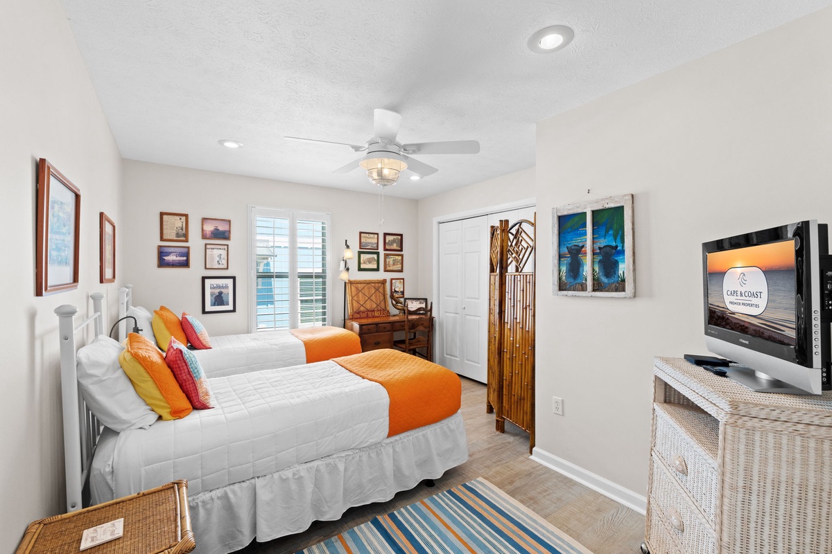 Bright coastal bedroom with twin beds, cheerful orange accents, and nautical art creating your perfect seaside retreat.