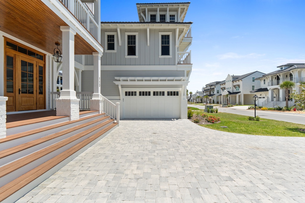 Modern coastal home with covered front porch and paver driveway in peaceful neighborhood setting.