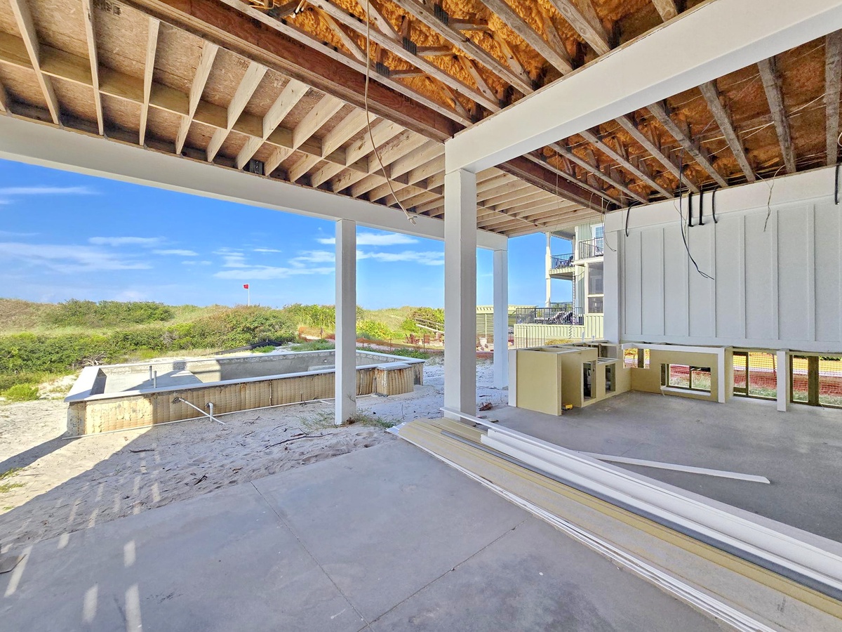 A covered terrace space offers open views of coastal dunes and natural vegetation, with modern architecture framing the beachside setting beyond.