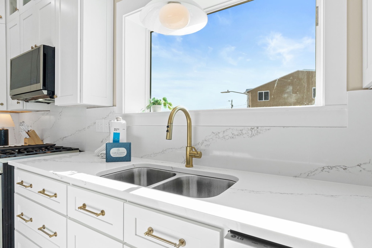 Your bright modern kitchen invites culinary adventures with gleaming countertops, brass fixtures, and natural light streaming through windows.