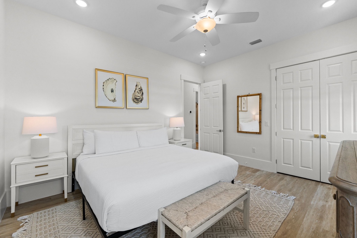 Unwind in your serene bedroom featuring crisp white linens, coastal artwork, and a gentle ceiling fan for perfect comfort.