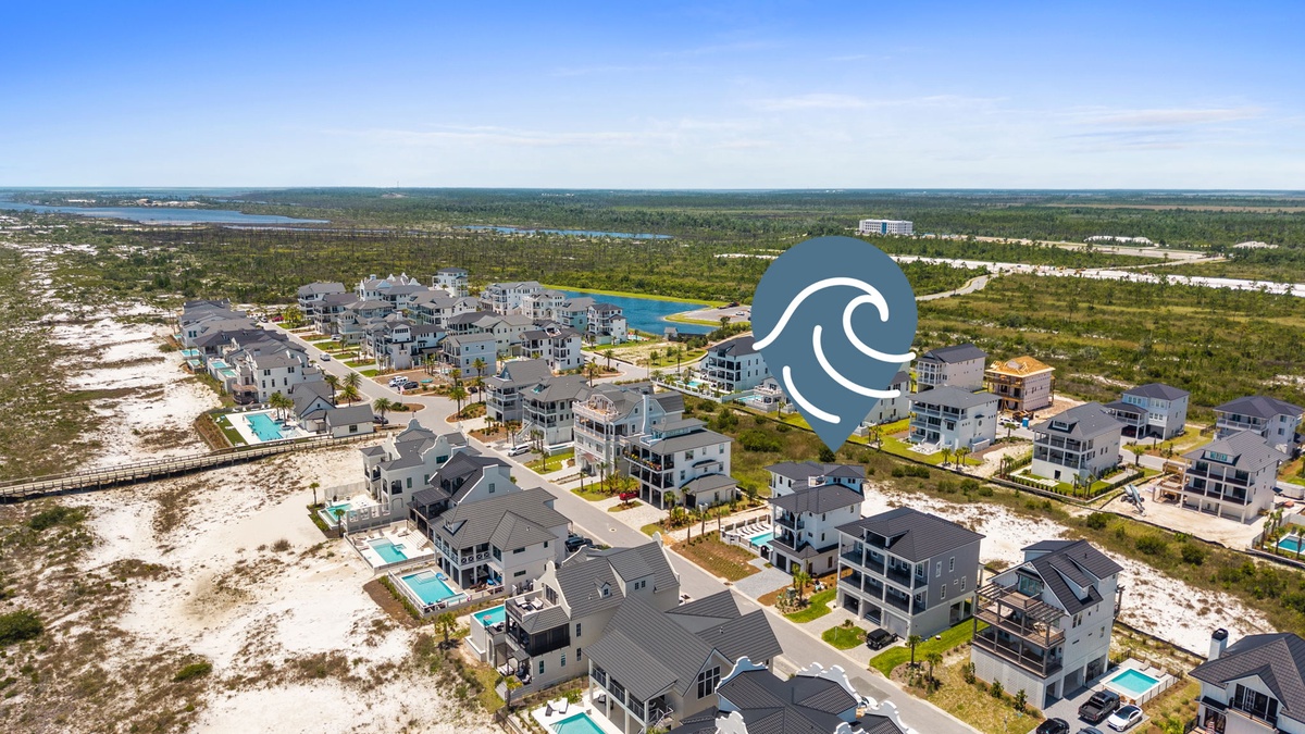 An aerial perspective of a coastal vacation community featuring modern beach homes, private pools, and direct access to pristine white sand beaches and scenic waterways.