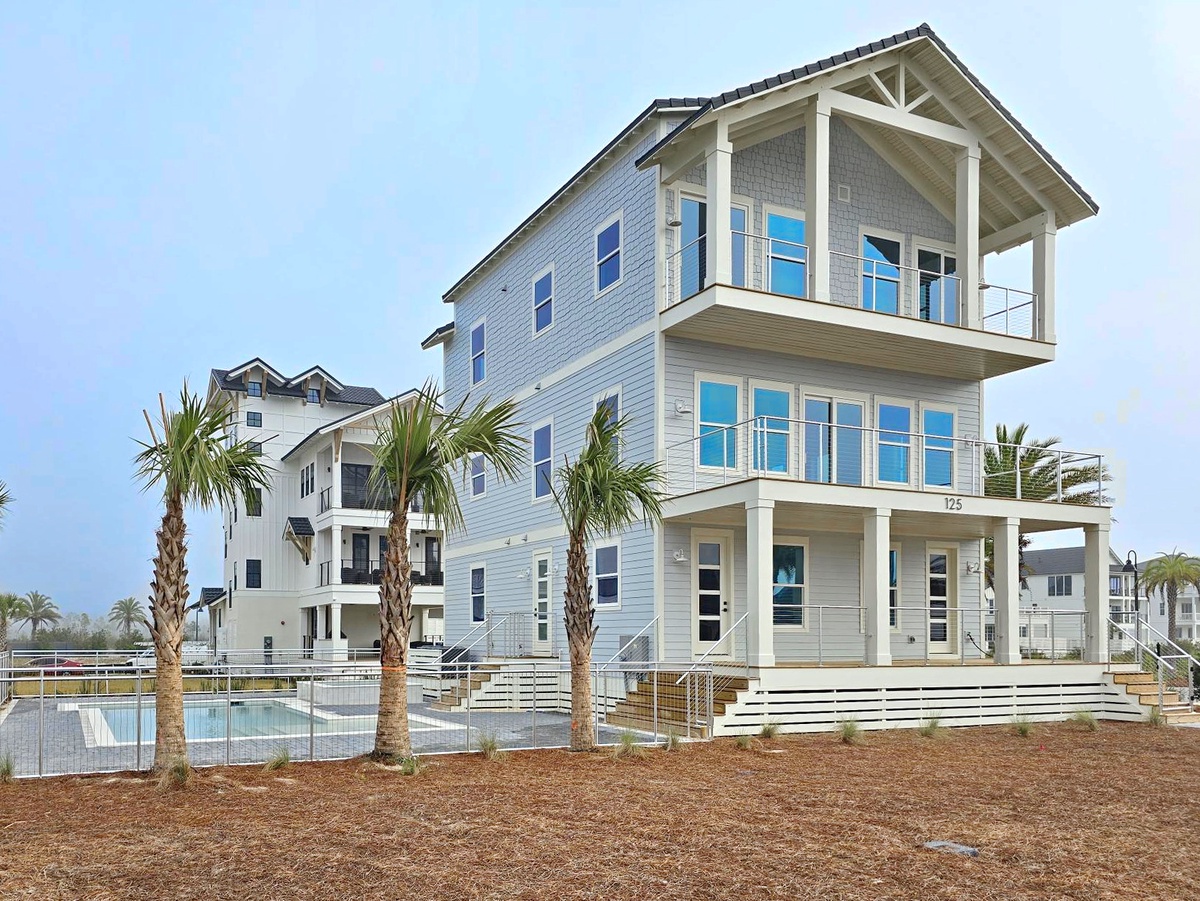 Modern coastal home with palm trees and swimming pool in beachside community setting.