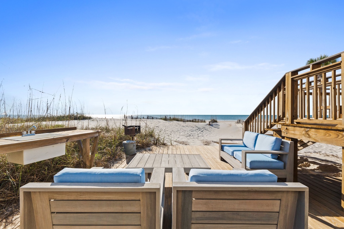Wooden deck overlooking pristine white sand beach with comfortable loungers and ocean views.