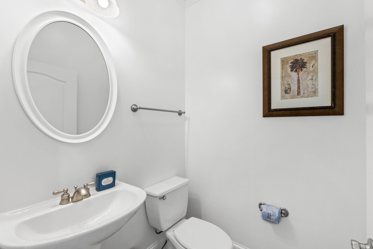 Your private powder room features a classic pedestal sink, round mirror, and coastal-inspired décor—a clean, bright space designed for your comfort and convenience.