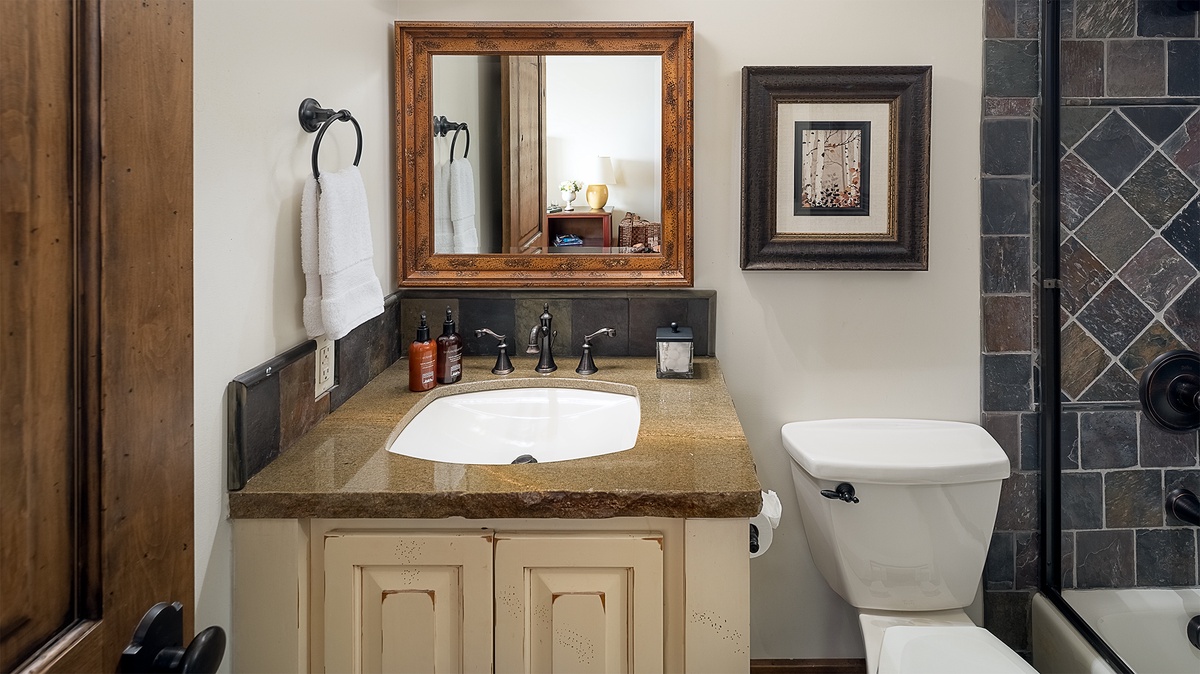 Your private bathroom features a granite vanity, framed mirror, fresh towels, and decorative tile details—everything set for a relaxing retreat.