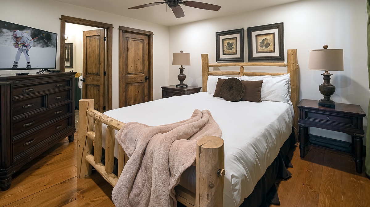 Your cozy retreat features a plush bed with rustic wood accents, flanked by elegant nightstands and soft lighting. Unwind with your favorite shows on the flat-screen TV after a day of adventure.