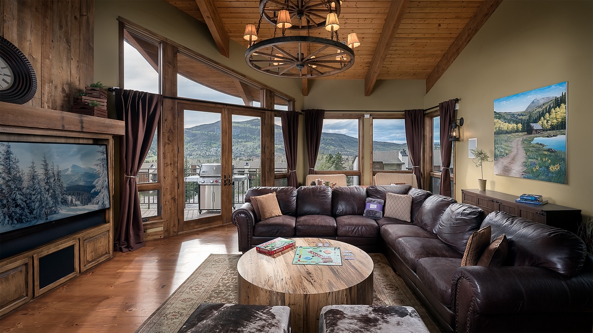 Relax in your spacious living room with soaring ceilings, a rustic wagon-wheel chandelier, and plush leather sectional. Floor-to-ceiling windows frame stunning mountain views, while warm wood accents create a cozy retreat.
