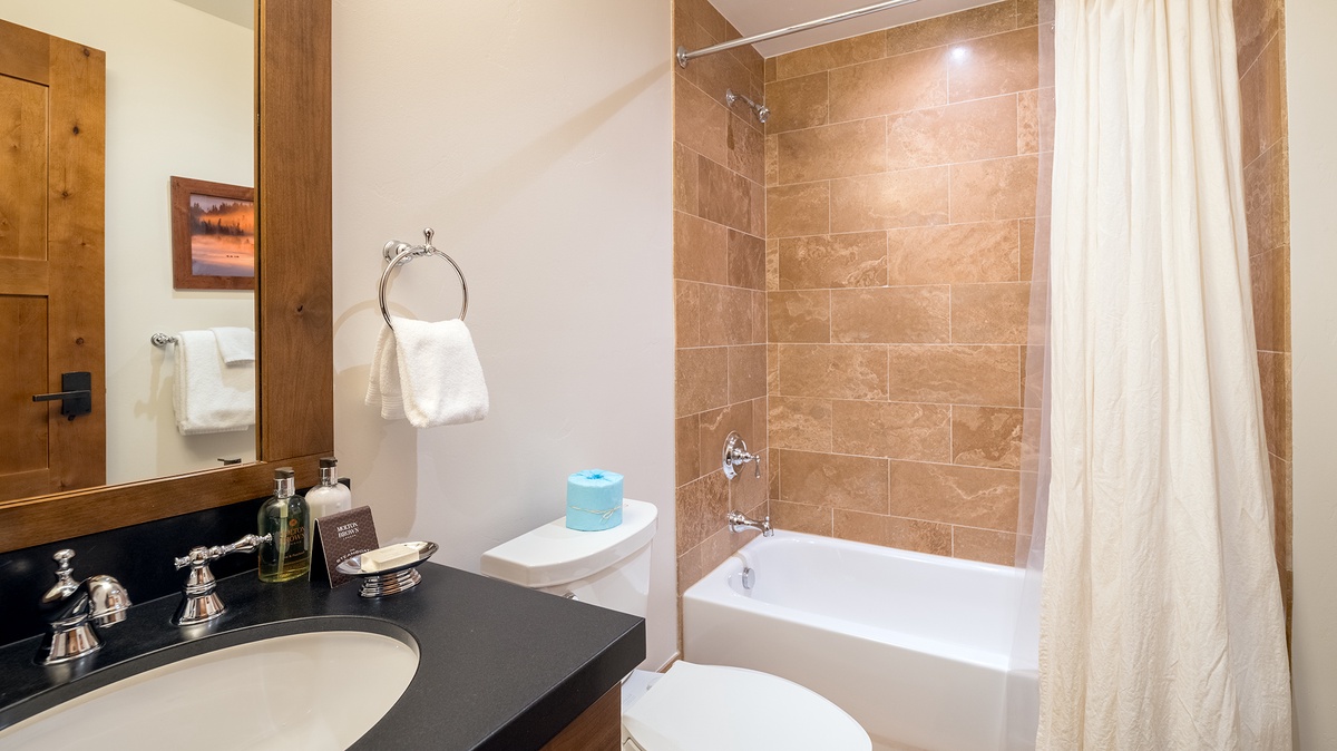 A pristine bathroom features warm travertine tile, a deep soaking tub, and a polished vanity with thoughtful touches—your private spa awaits.