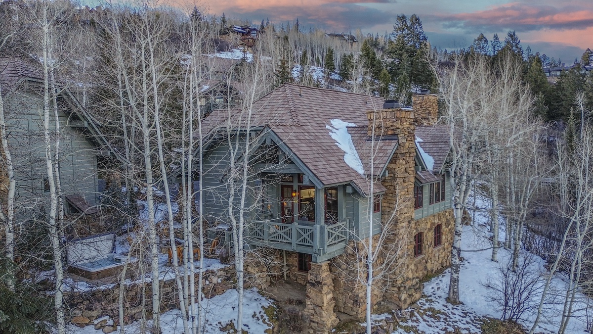 Stunning mountain retreat with stone architecture nestled among snow-dusted aspens and evergreens during golden hour twilight.