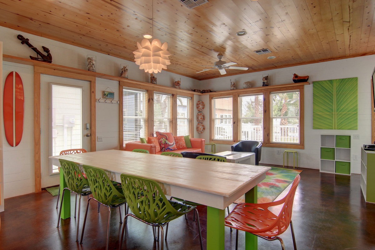 Your bright dining space features modern green chairs and colorful coastal decor under warm wood ceilings with natural light streaming in.