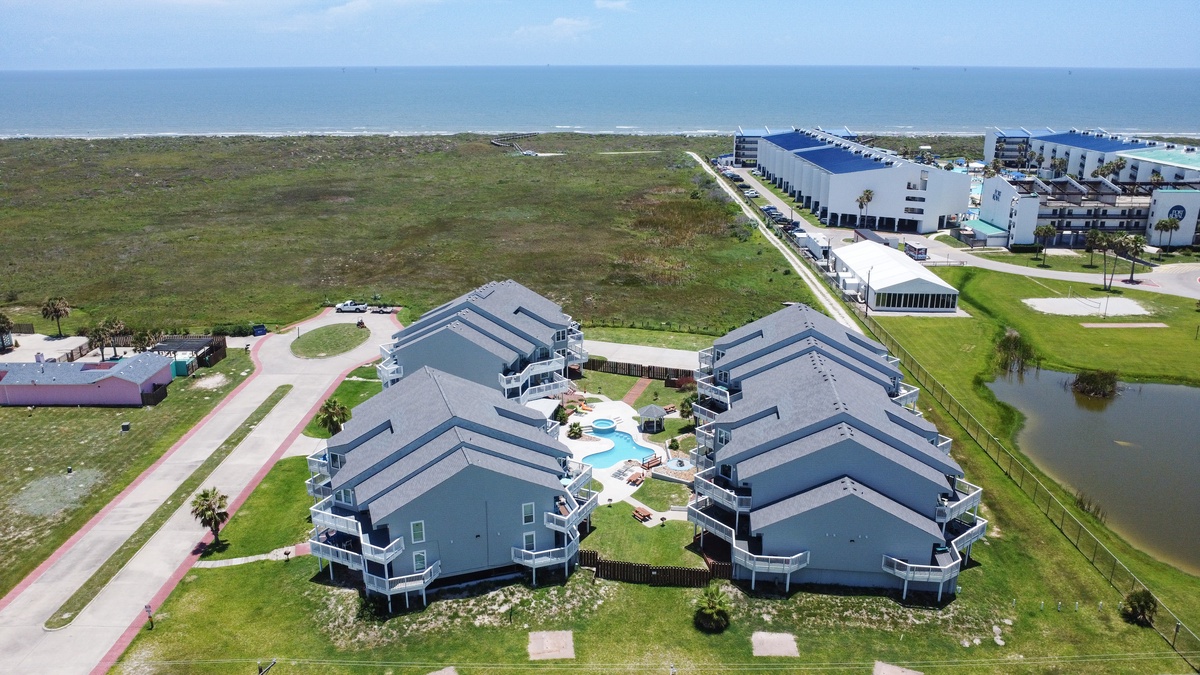Coastal resort complex with swimming pools situated between oceanfront and inland waterway, surrounded by natural dunes and residential developments.