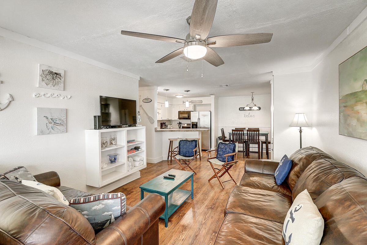 Relax in your spacious open-concept living room with comfy leather seating, coastal artwork, and kitchen views perfect for socializing.