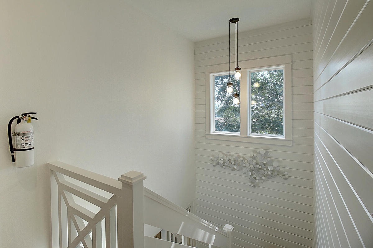 Step into this bright staircase landing where natural light streams through the window, illuminating clean white walls and charming shiplap details.