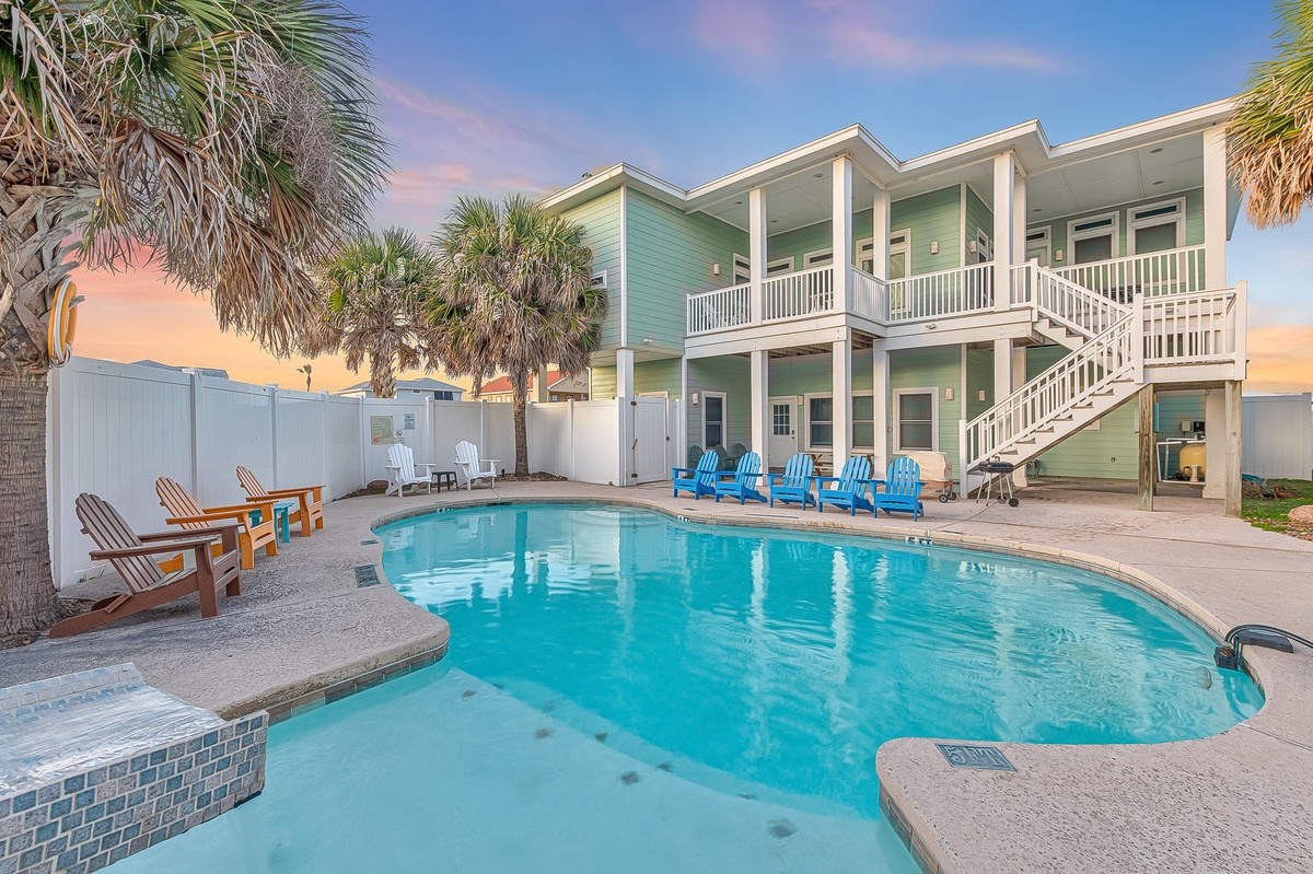 Stunning two-story coastal property featuring private pool, tropical palms, and vibrant turquoise exterior under colorful sunset skies.