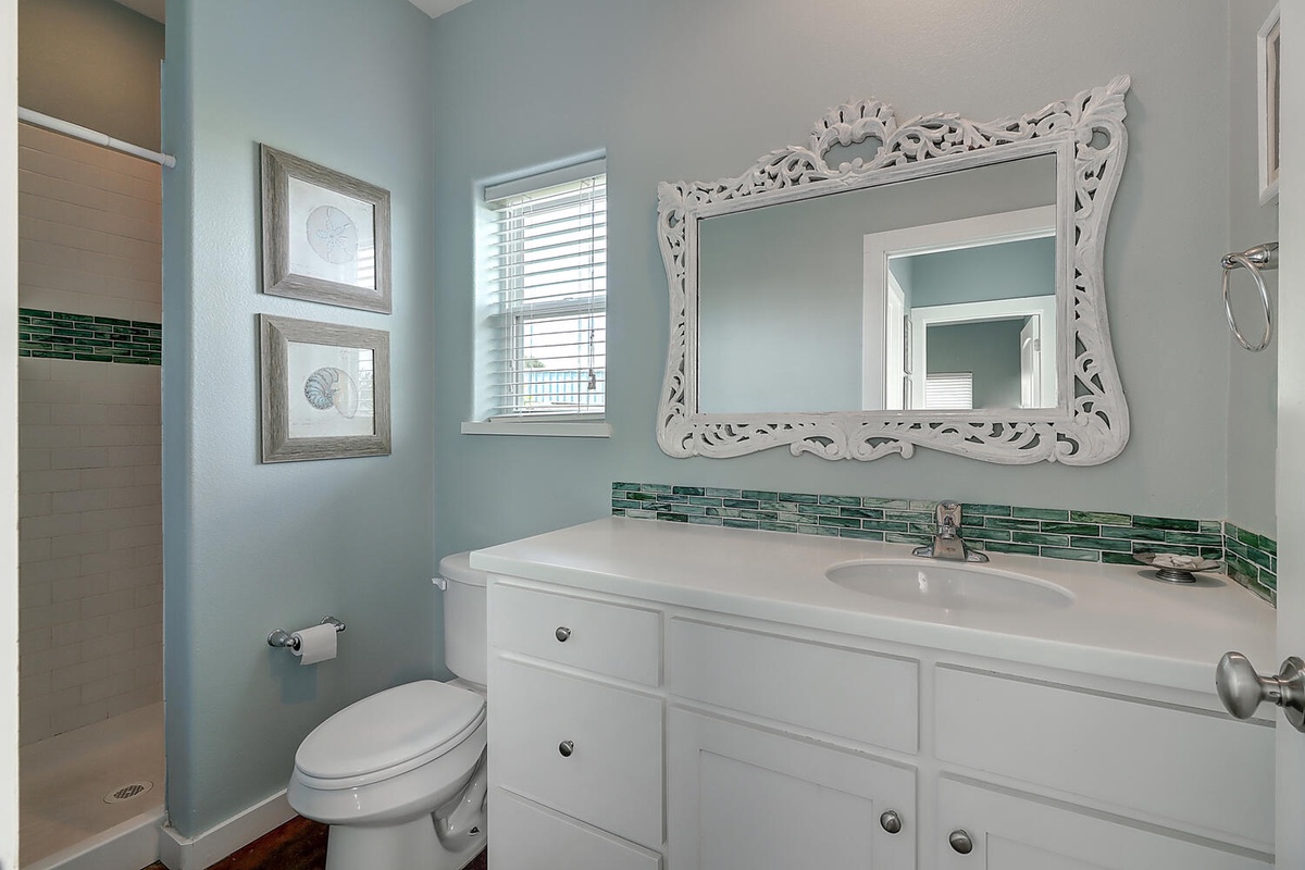 Refresh in your elegant bathroom featuring coastal-inspired turquoise walls, decorative mirror, and stunning green glass tile accents.