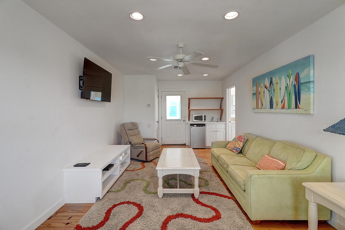 Relax in your bright, airy living space with a plush green sofa, entertainment center, and cheerful surfboard art that perfectly captures the coastal vibe.