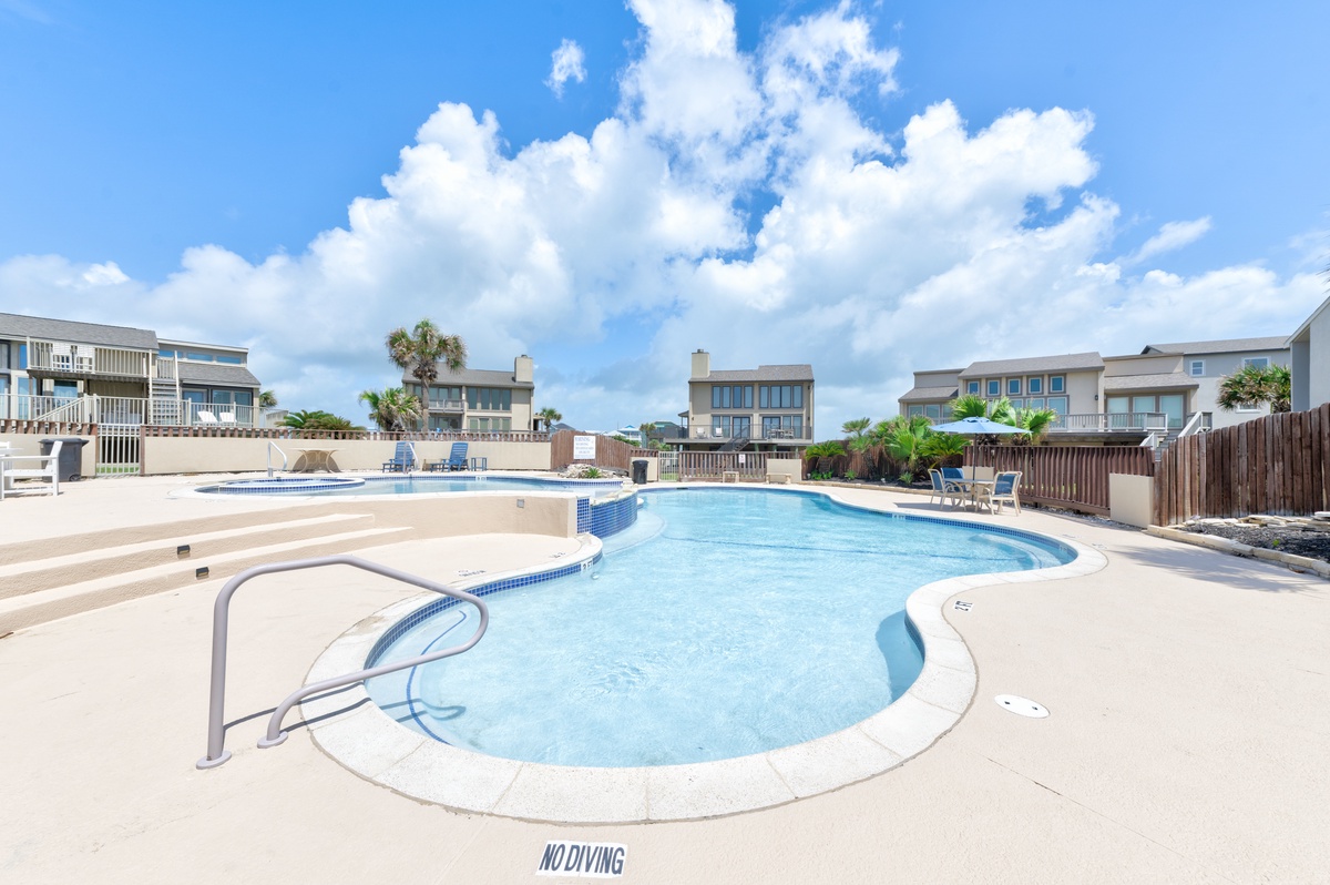 A beautiful community swimming pool surrounded by vacation homes under bright blue skies with fluffy white clouds.