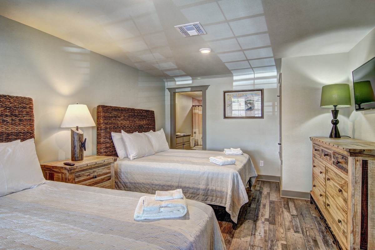 Unwind in your cozy bedroom featuring two comfortable beds with rustic woven headboards, soft linens, and warm wood furnishings.