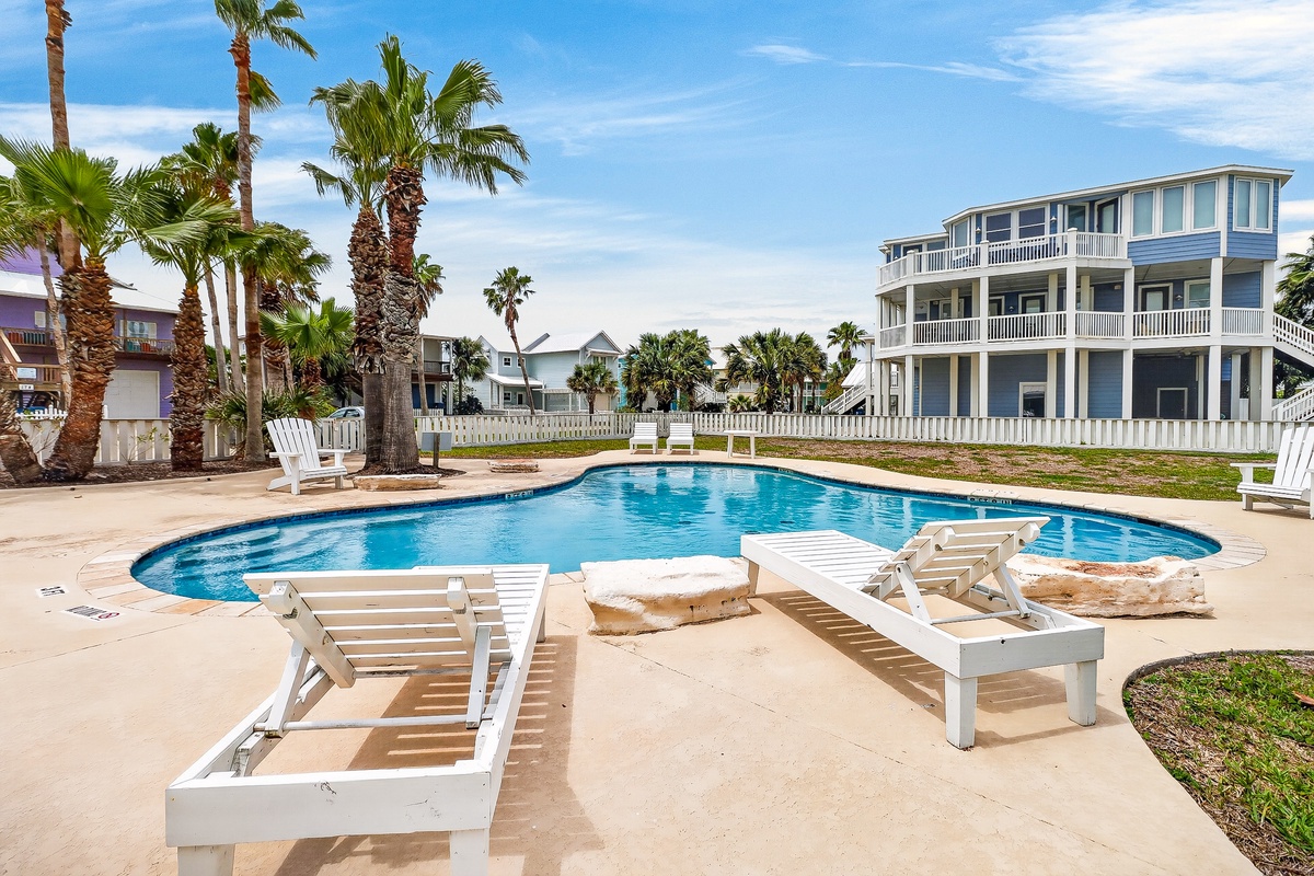 Coastal community pool area surrounded by palm trees and beach houses, offering shared amenities for the neighborhood.