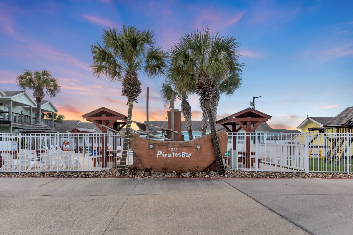 Welcome to Pirates Bay, where tropical palm trees frame the entrance to this coastal community under stunning sunset skies.