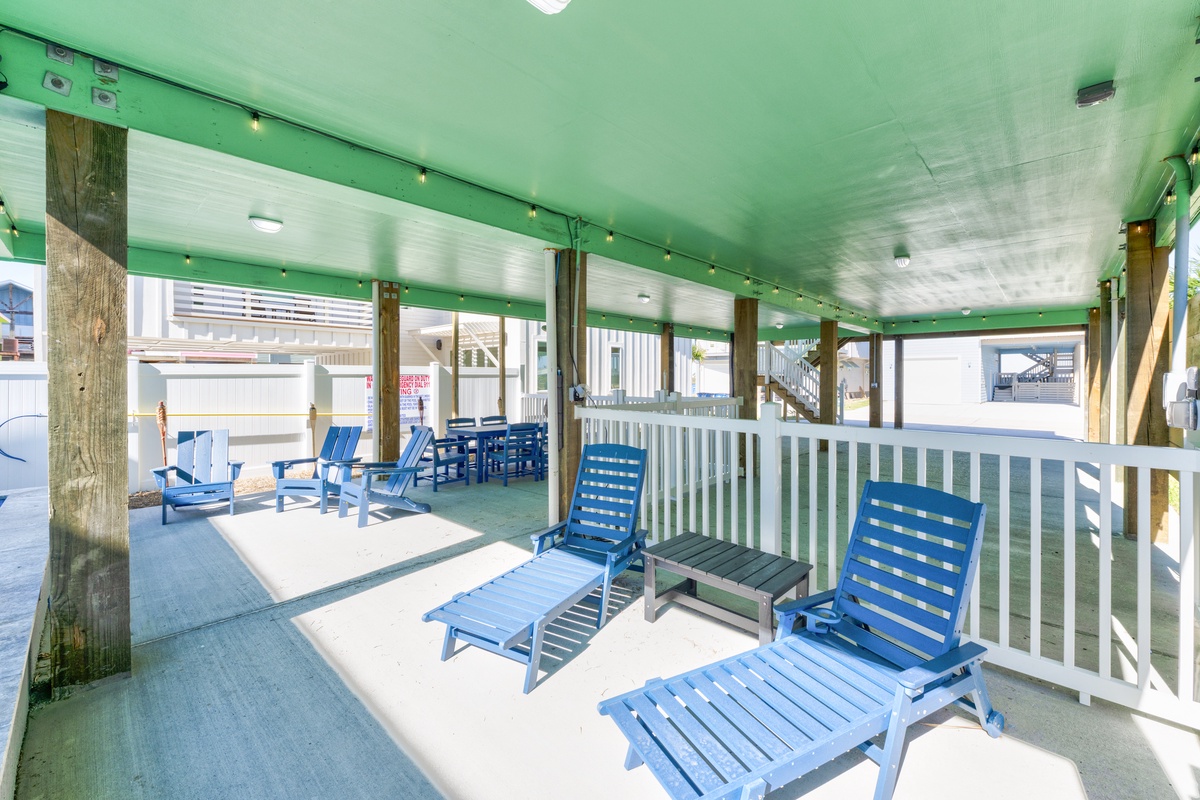Relax on your expansive covered deck with bright blue lounge chairs and ocean breezes flowing through this cheerful coastal retreat.