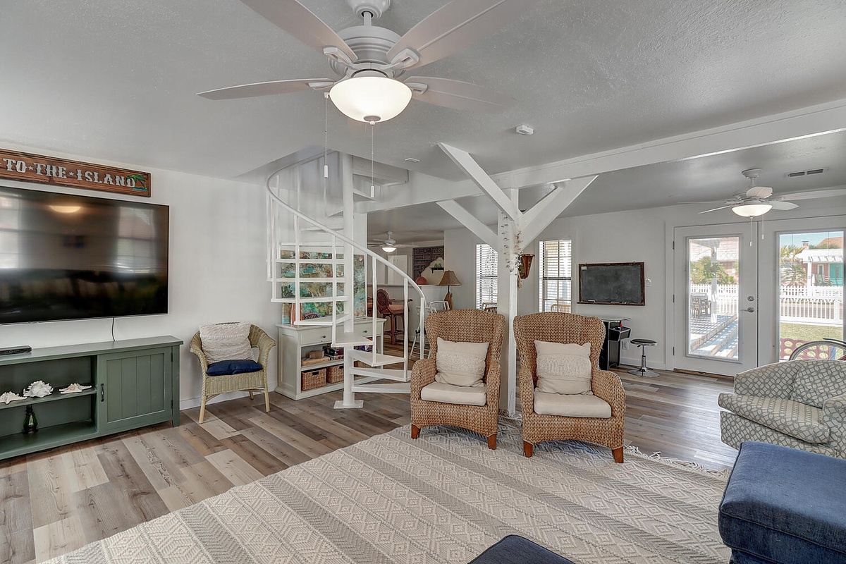 Relax in your coastal-inspired living space with comfortable wicker chairs, entertainment center, and breezy ceiling fans for perfect comfort.