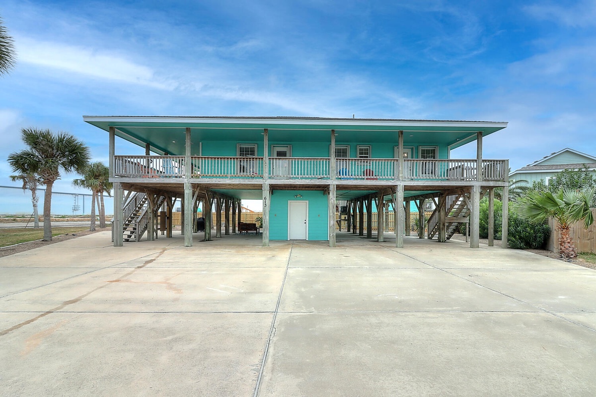 Charming turquoise beach house on stilts with wraparound deck and convenient ground-level parking in a tropical coastal setting.