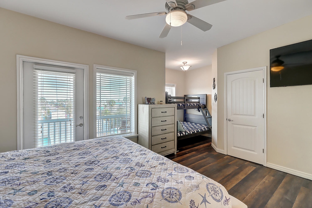 Your spacious bedroom features a queen bed and bunk beds, perfect for families. Natural light fills the room through large windows.
