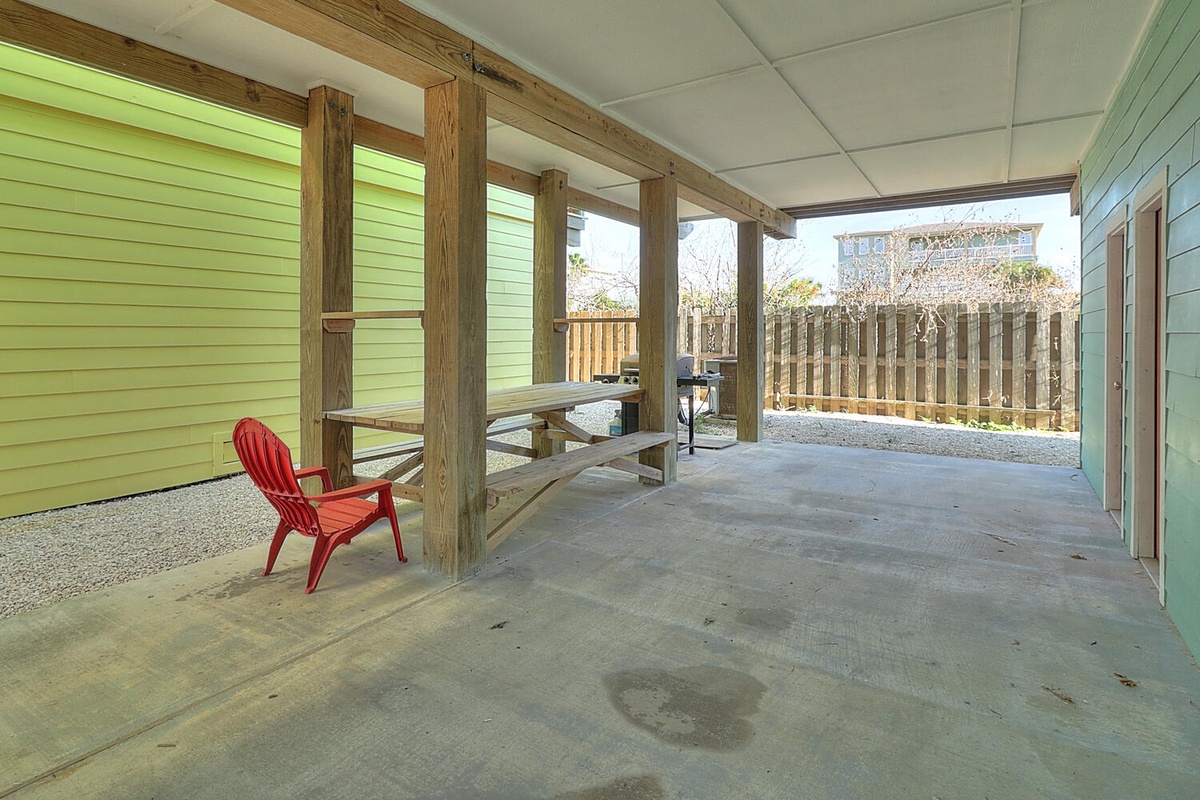 Relax in your private covered patio with rustic wooden beams, featuring a bright red Adirondack chair and picnic table for outdoor dining.