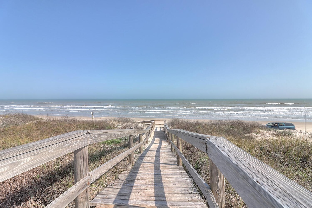 Wooden boardwalk leads directly to pristine sandy beach with rolling waves and endless ocean views.