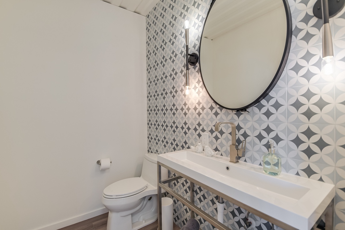 Fresh up in your stylish powder room featuring geometric wallpaper, sleek pendant lighting, and modern fixtures for your comfort.