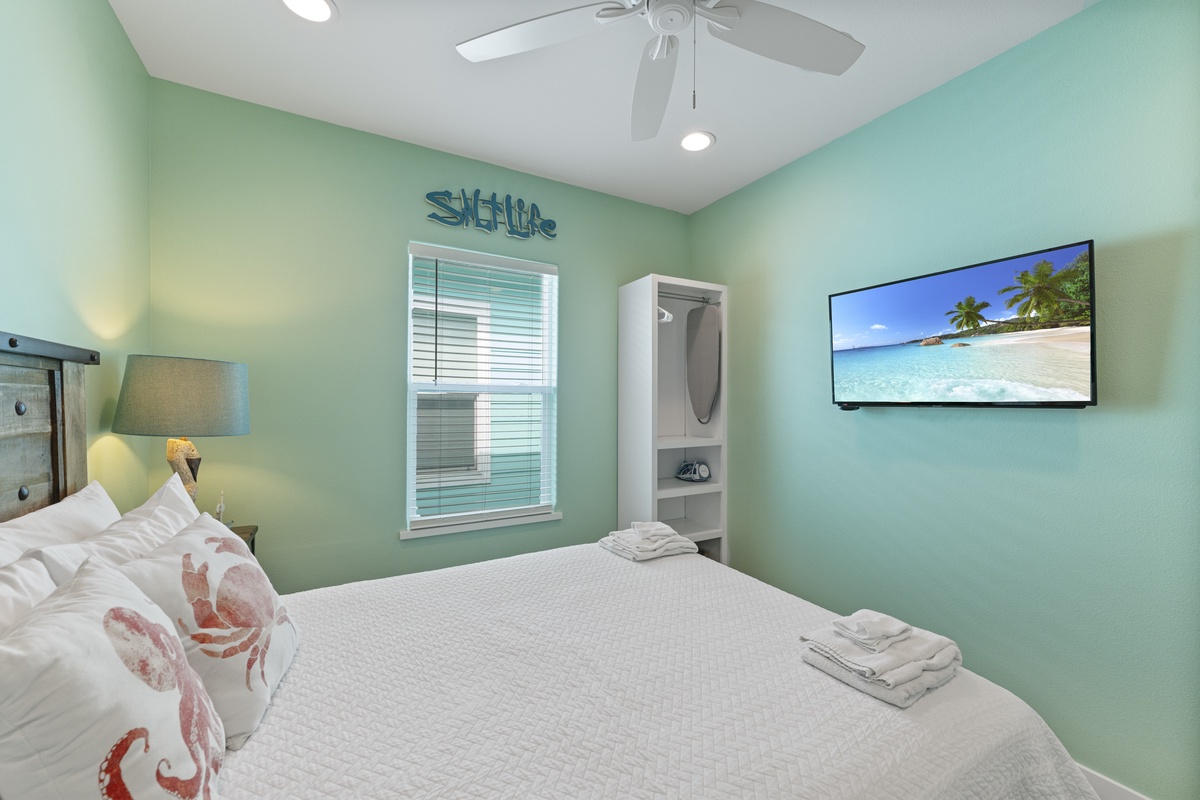 Your breezy coastal retreat awaits with soothing aqua tones, crisp white linens, and a gentle ceiling fan overhead to keep you comfortable all night long.