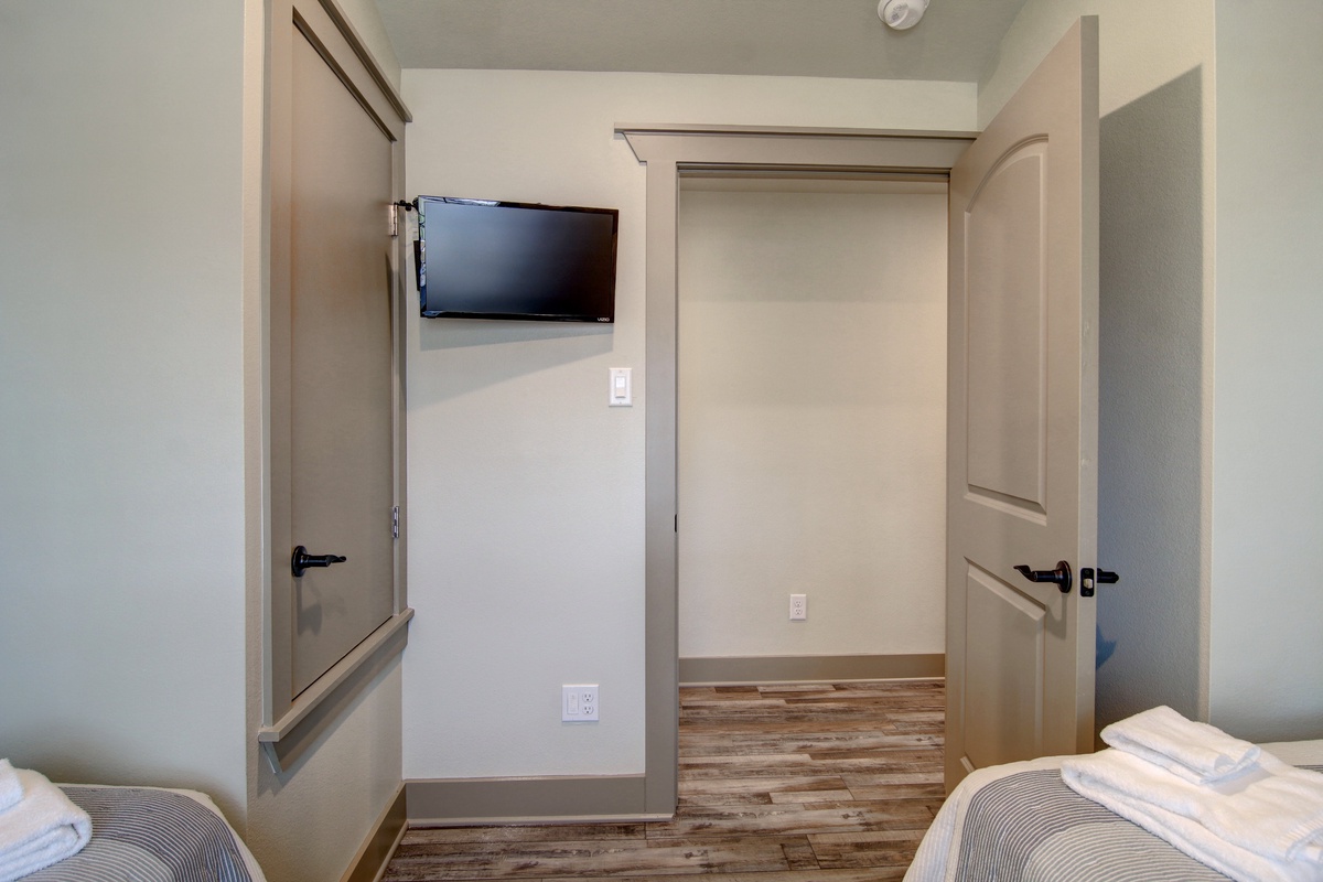 Your cozy bedroom features a wall-mounted TV and thoughtful storage solutions, with warm wood floors and neutral tones creating a peaceful retreat.