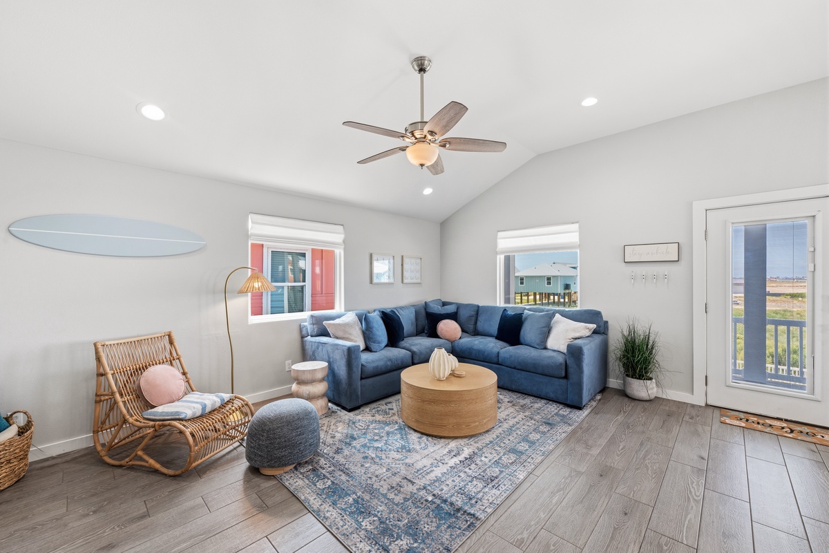 Settle into your coastal living room, where soft blues meet natural textures and vaulted ceilings create an airy escape. With the surfboard overhead and a rocking chair ready for lazy afternoons, you'll find your perfect spot to unwind.