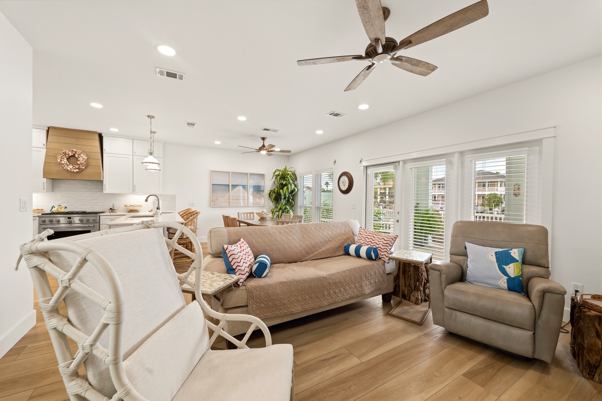Bright, coastal-inspired living space with vaulted ceilings, natural light, and plush seating. Ceiling fans and an open-plan layout flow into a modern kitchen—ideal for your beach getaway.