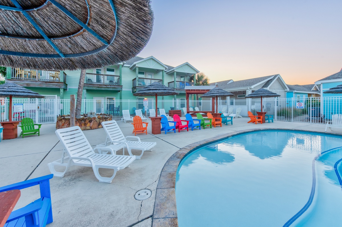 A tropical paradise awaits with sparkling pool, colorful Adirondack chairs, and charming beach cottages creating your perfect coastal getaway.