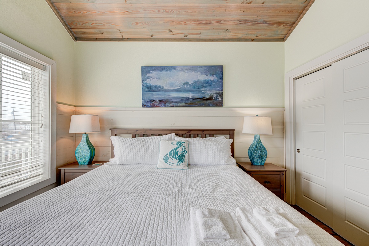 Drift off under beautiful wood ceilings in your serene bedroom, where coastal art and soft linens create the perfect peaceful retreat.
