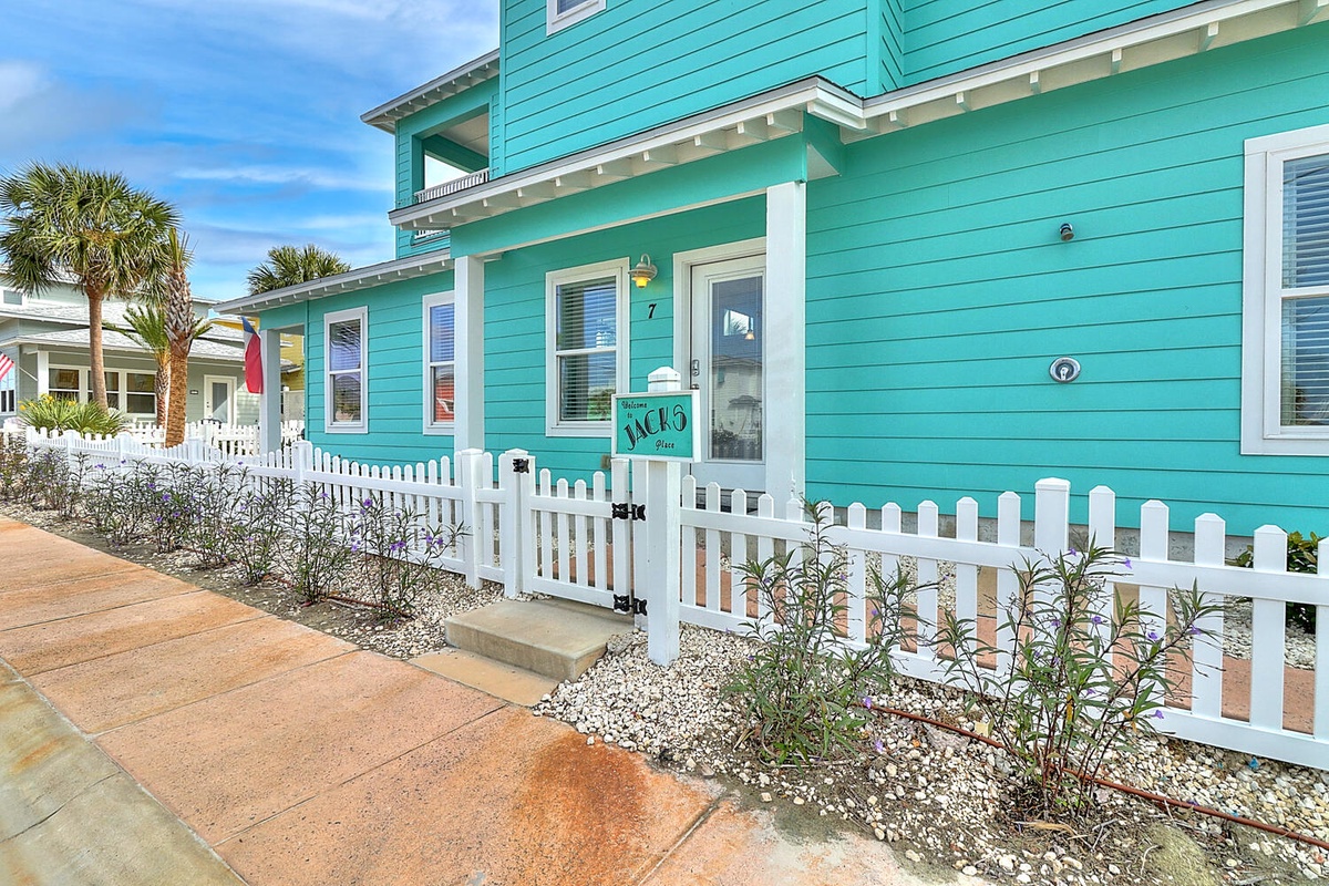 A charming turquoise beach cottage with white picket fence and tropical landscaping creates the perfect coastal getaway entrance.