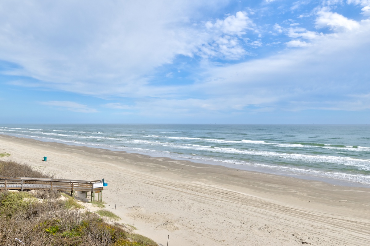 Pristine coastline stretches endlessly with rolling waves and soft sand dunes creating a peaceful seaside setting.