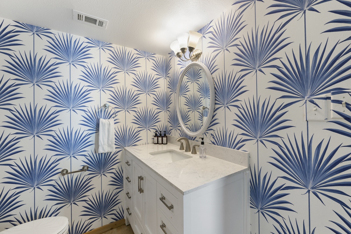 Freshen up in your private bathroom featuring bold tropical palm wallpaper, a marble vanity, and thoughtful amenities—a bright, stylish retreat for your stay.