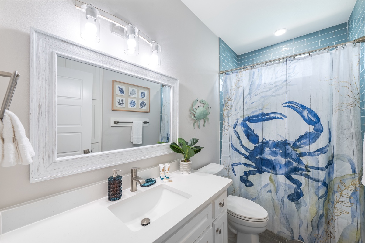 Your coastal bathroom features ocean-themed decor with vibrant blue crab artwork, creating a beachside retreat where you'll feel refreshed.